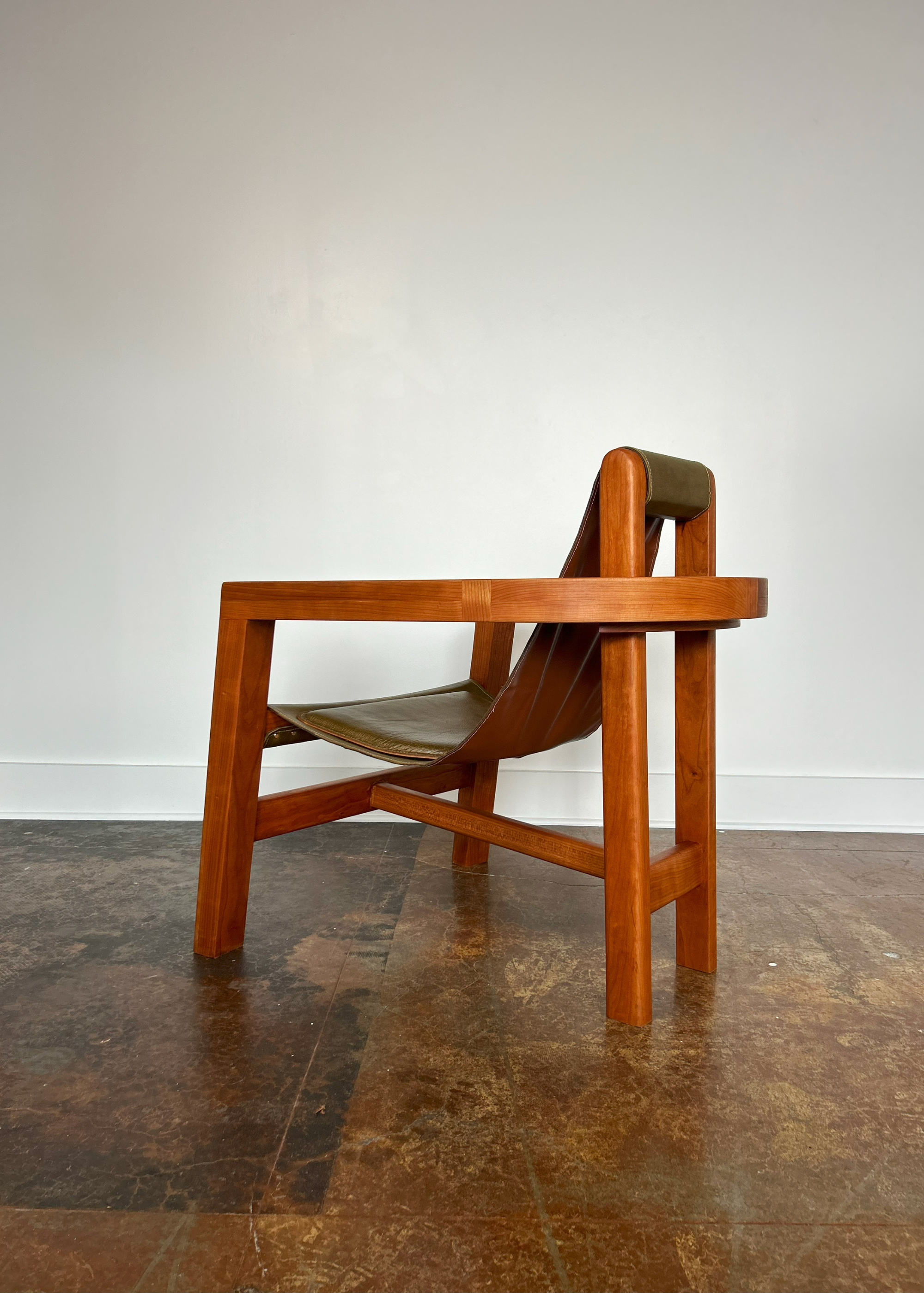 A wood chair with a leather seat in a white room with stone flooring