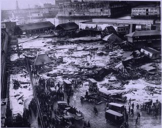 In 1919, a collapsed molasses tank sent a towering wave of the sticky mess through the streets, ensnaring everything from humans to horses to homes. The wreckage of the tank can be seen in the upper-right of the image. 