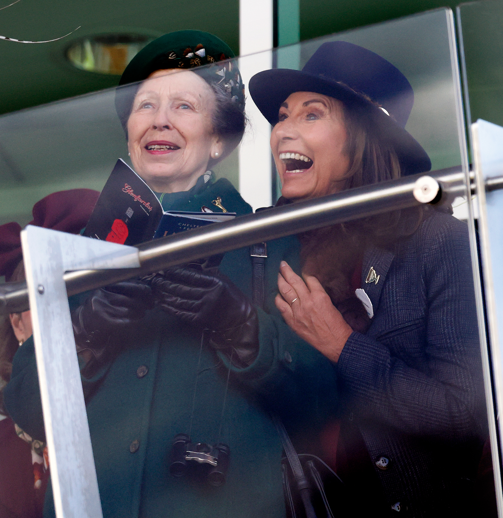 Carole Middleton hugging Princess Anne, who is holding a racing booklet
