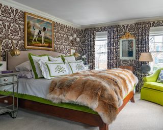A master bedroom with ornate brown and white wallpaper, green and white bedding, a lime green armchair and a painting of a dog over the headboard