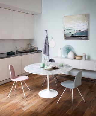 Pictures of kitchens with wooden flooring, round dining table and pastel colored chairs.