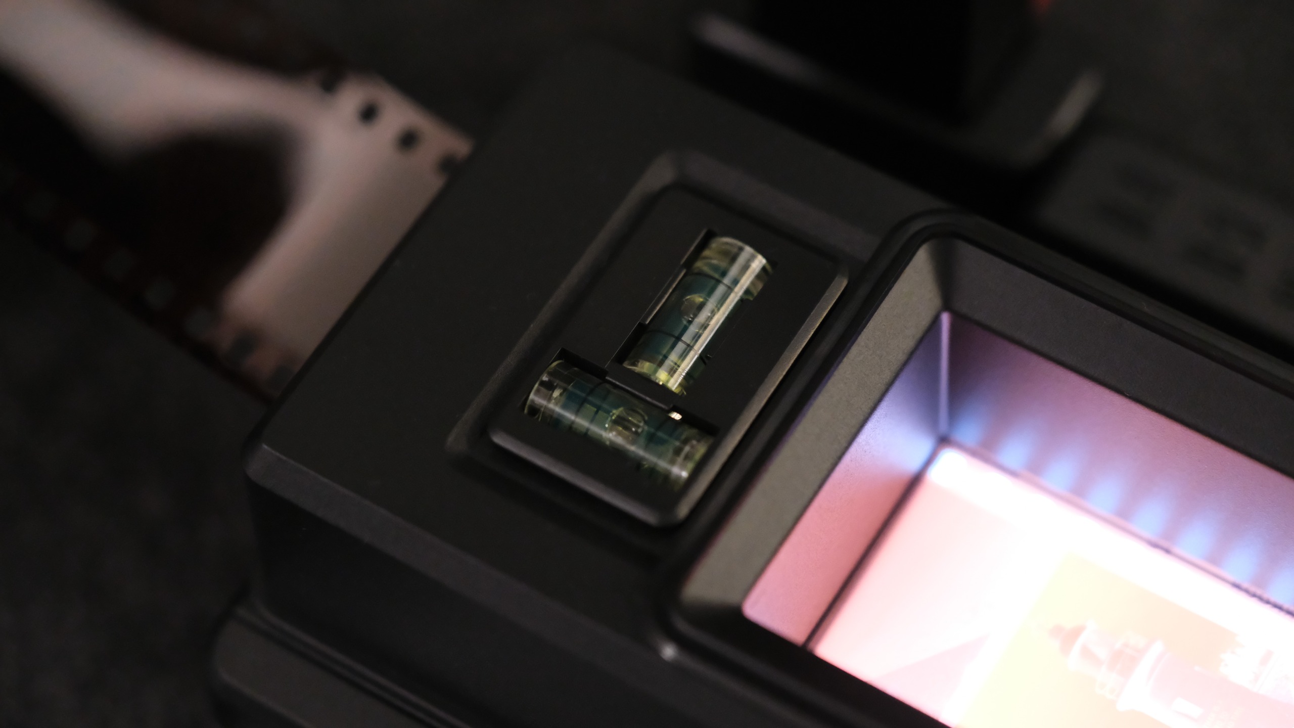 A close-up of two small, cylindrical green bubble levels integrated into the black plastic casing of a film scanning device, positioned immediately next to a brightly illuminated film viewing window.
