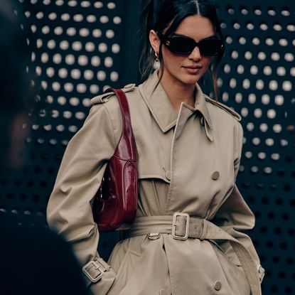 Kendall Jenner wearing a tan trench coat with a red handbag