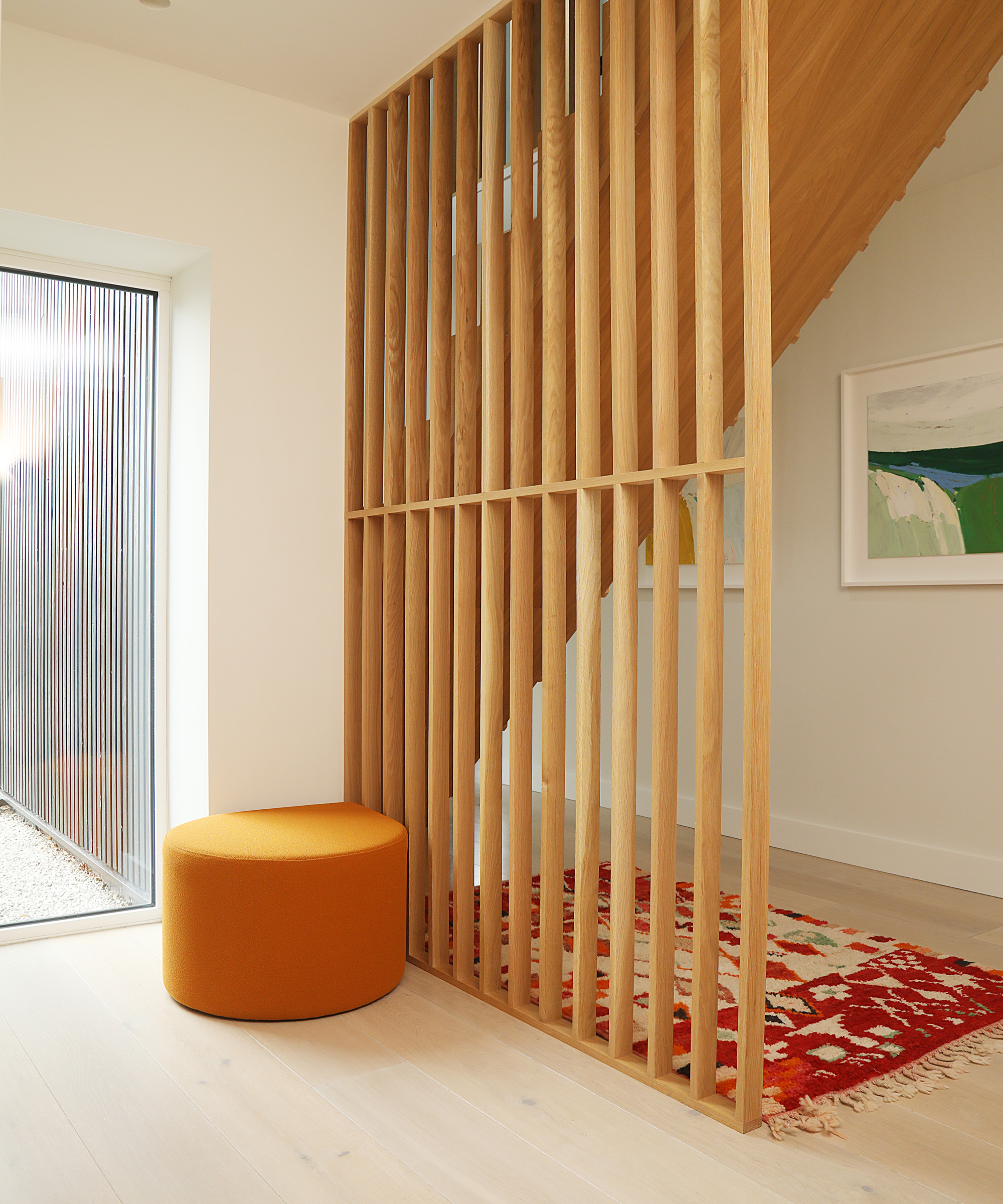 A hallway with light flooring and a bespoke timber rail coming from the staircase