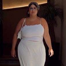 Influencer standing in front of doorway with white two-piece linen set, sunglasses, and white shoulder bag.