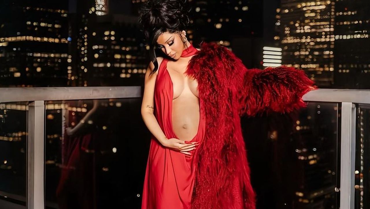 Cardi B stands on a balcony in Manhattan wearing a red cutout gown and red fur coat