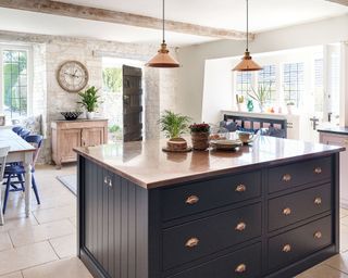 Shaker style country kitchen with dark blue island and copper worktop and lights in 12th century Cotswolds country house