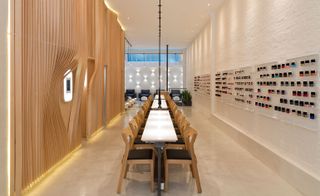 Inside the open-place space featuring a painted white brick and light wood wall, three narrow tables with 8 seats at each bench.