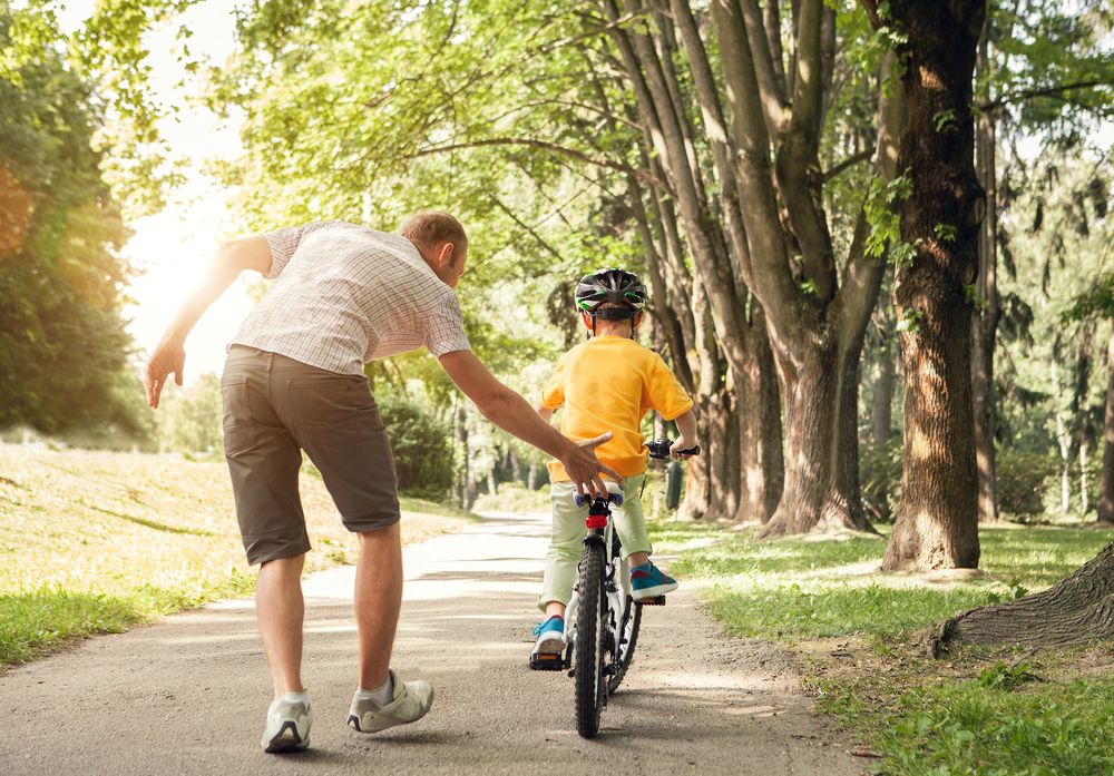 A dad helps his son learn to ride a bike.