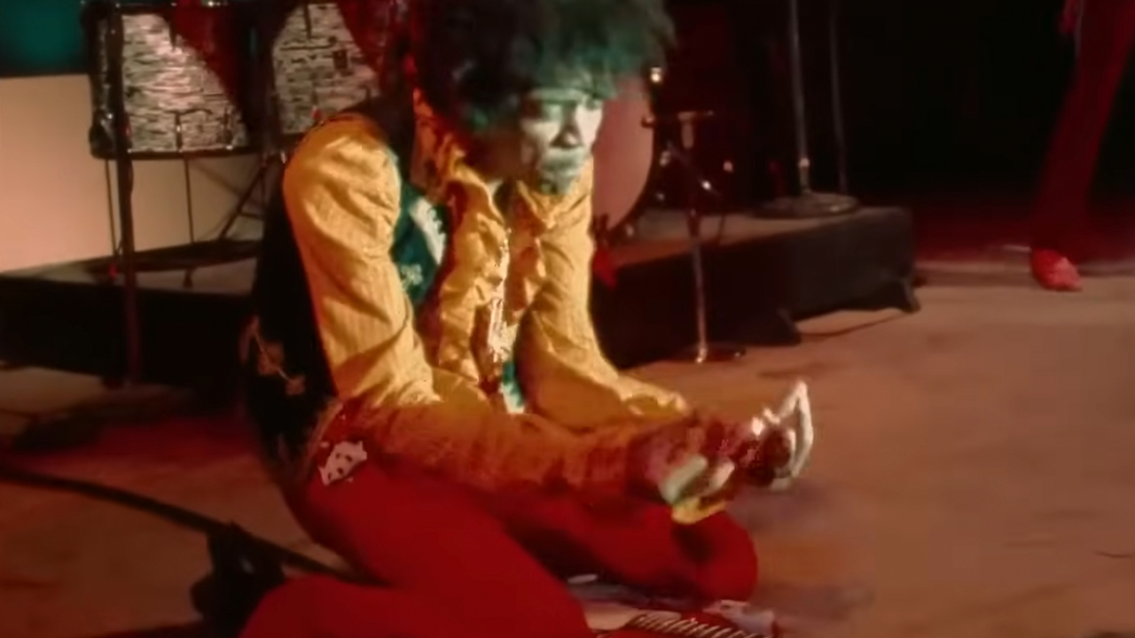 Jimi Hendrix kneeling behind his guitar, looking like he is praying