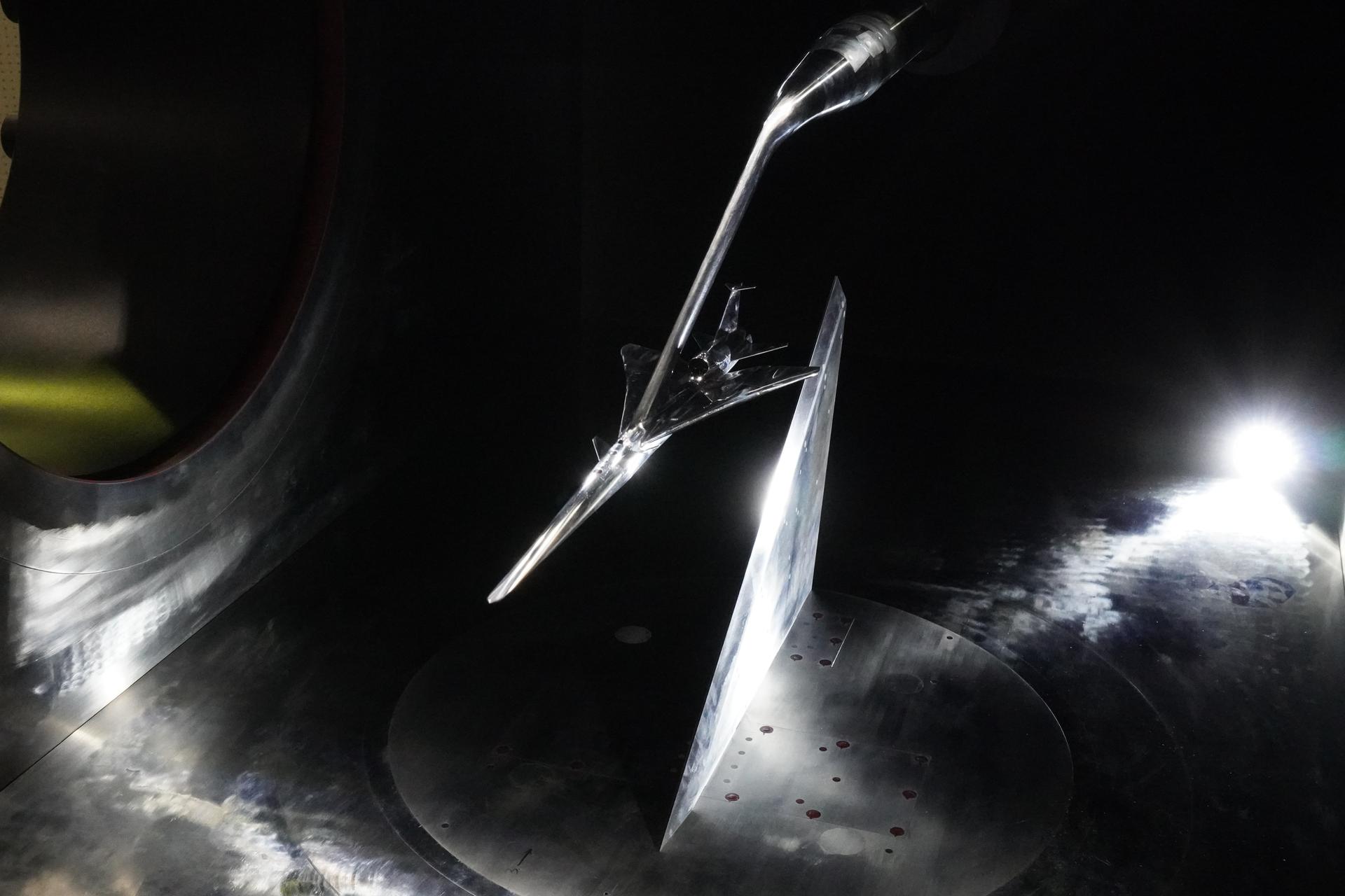 A metal model of a plane floats in a dark wind tunnel