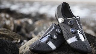 A pair of black Bont Vaypor S shoes sit on a rock on a beach