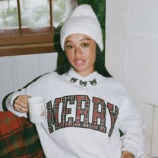 Young woman with freckles wearing Abercrombie 'Merry' sweatshirt and hat, holding a mug.