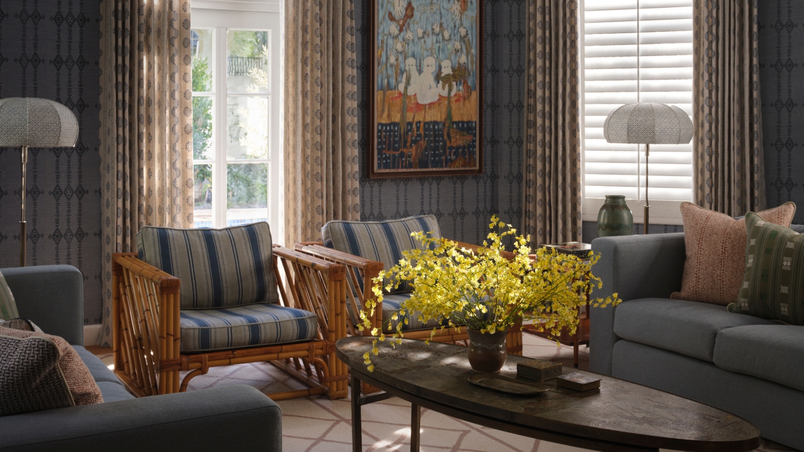 Living room with blue patterned walls, gray sofas, striped bamboo armchairs, antique coffee table and layered artwork.