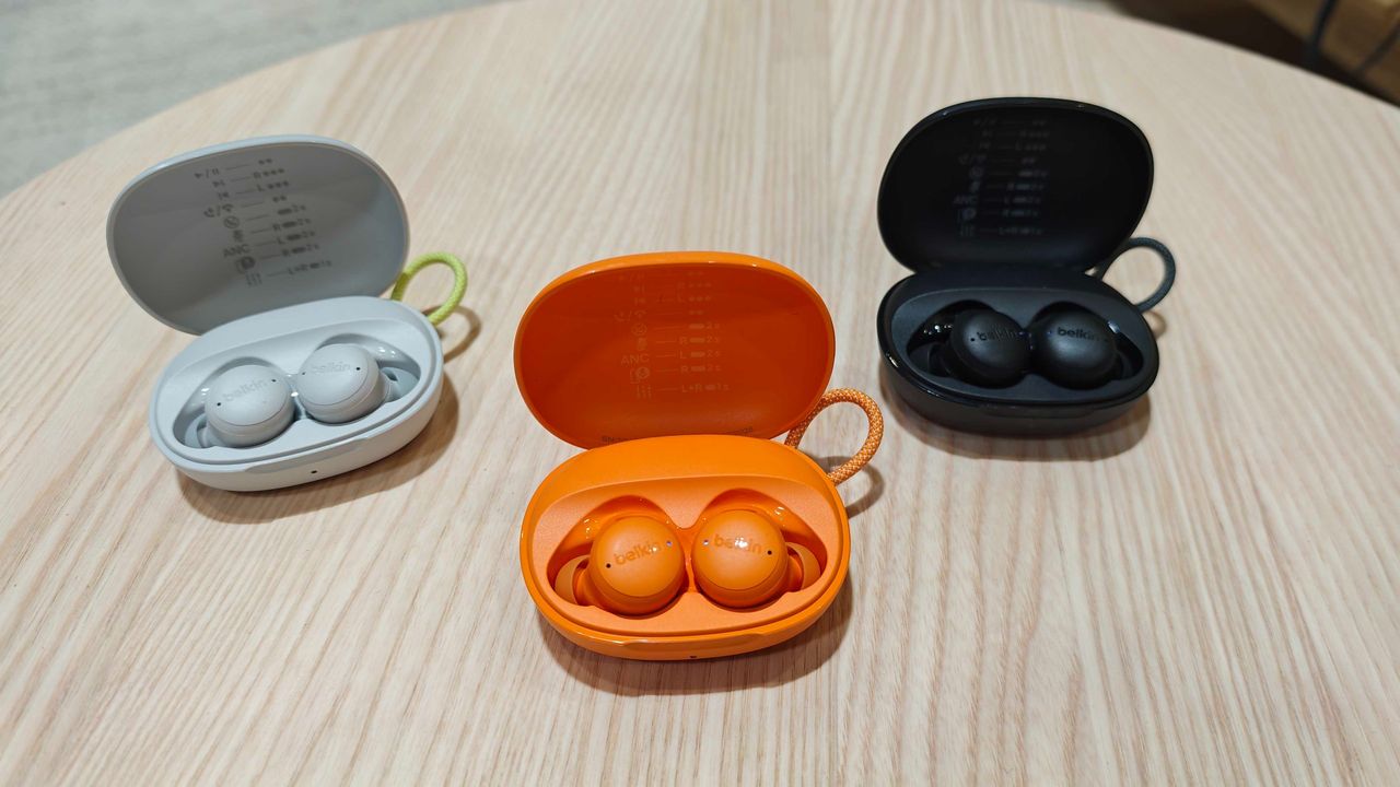 Belkin SoundForm Isolate Buds in orange and in a man's hand, with a wooden table in the background
