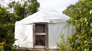 A white yurt in a back garden with a wooden door