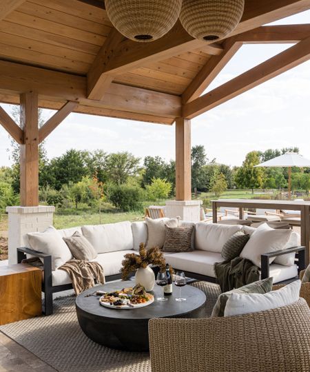 outdoor living room under a wooden roof with a corner sofa, black wooden coffee table, wicker chairs, cushions and throw blankets