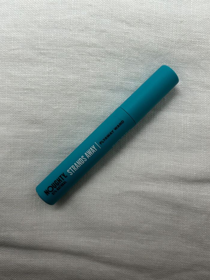 The Noughty Frizz Magic Flyaway Taming Wand on a white linen background