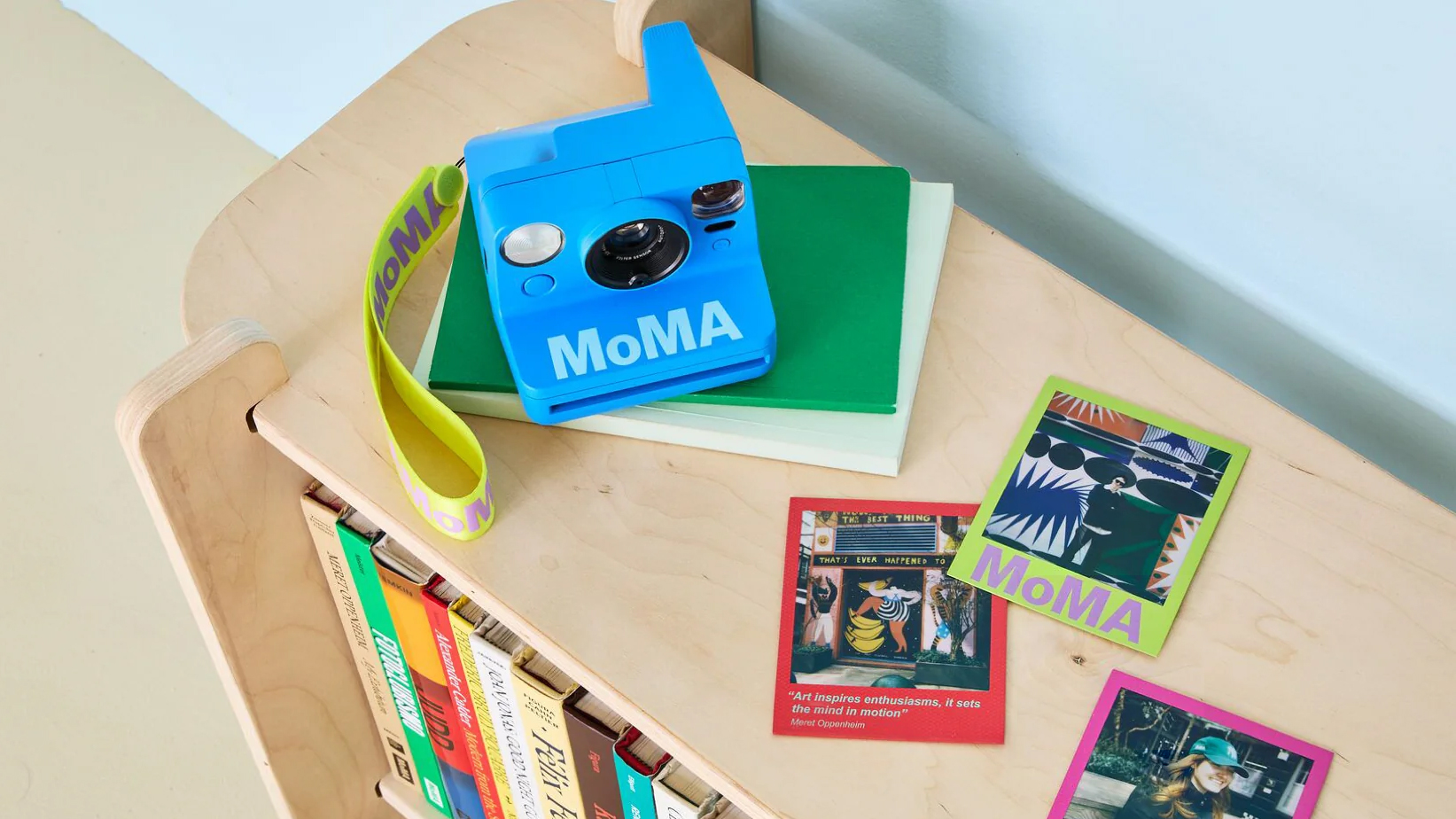 Polaroid Now Generation 3 – MoMA Edition and film on top of a wooden bookcase