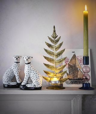 mantel with objet d'art, fern leaf tealight, candlestick with green candle, artwork and a pair of ceramic dalmations