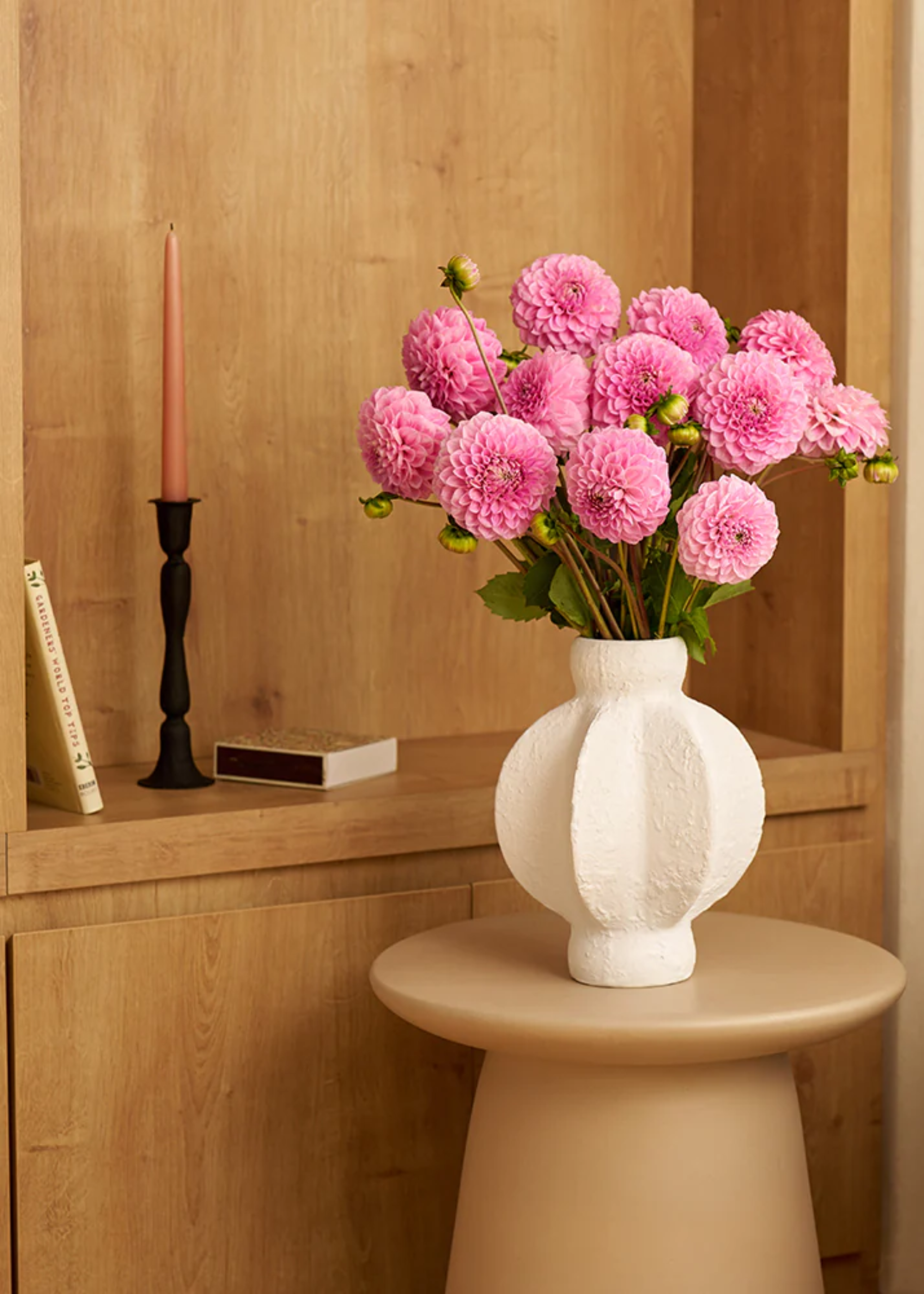 A textured white vase with pink dahlias on a beige stool