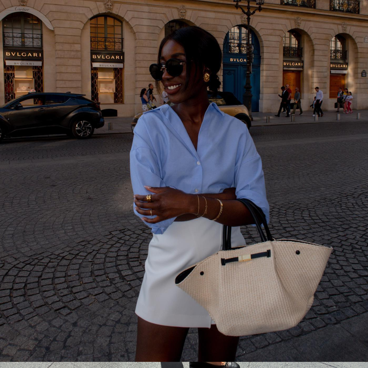 Aida wears a blue shirt, white skirt and raffia woven bag.