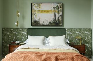 green bedroom with green velvet headboard, extended fabric covered headboard, artwork on wall, hanging pendant above one side table and a table lamp on the other