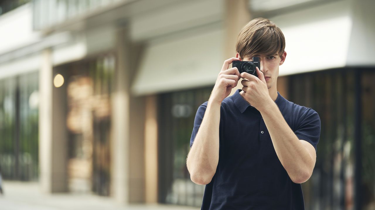 A man standing in the street, taking a picture with the best point and shoot camera