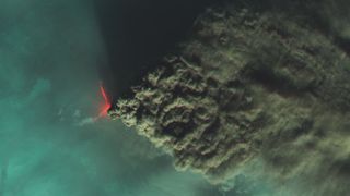 a volcano belches out a huge column of smoke, as seen from overhead