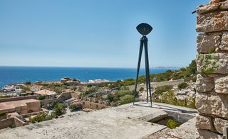Bronze sculpture on a concrete base on a hillside overlooking the sea