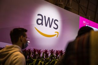 People walk in front of an Amazon Web Services sign on display on a conference floor