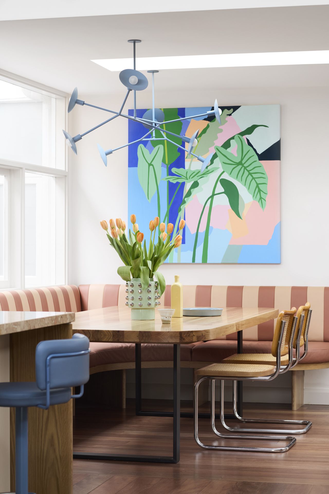 colorful banquette seating area off a kitchen with large artwork, blue pendant light, striped banquette seat and cesca chairs