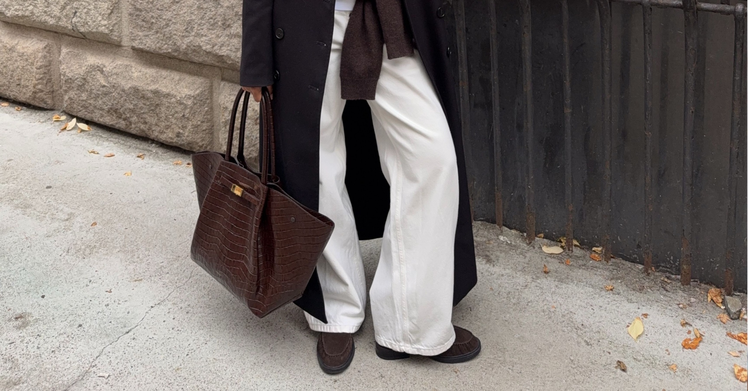 A content creator wears cream trousers with brown suede shearling-lined loafers and a brown bag