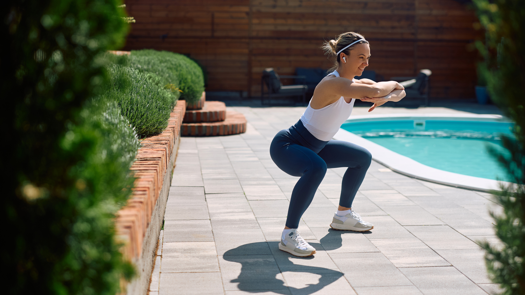 Woman doing the squat exercise outside next to a pool