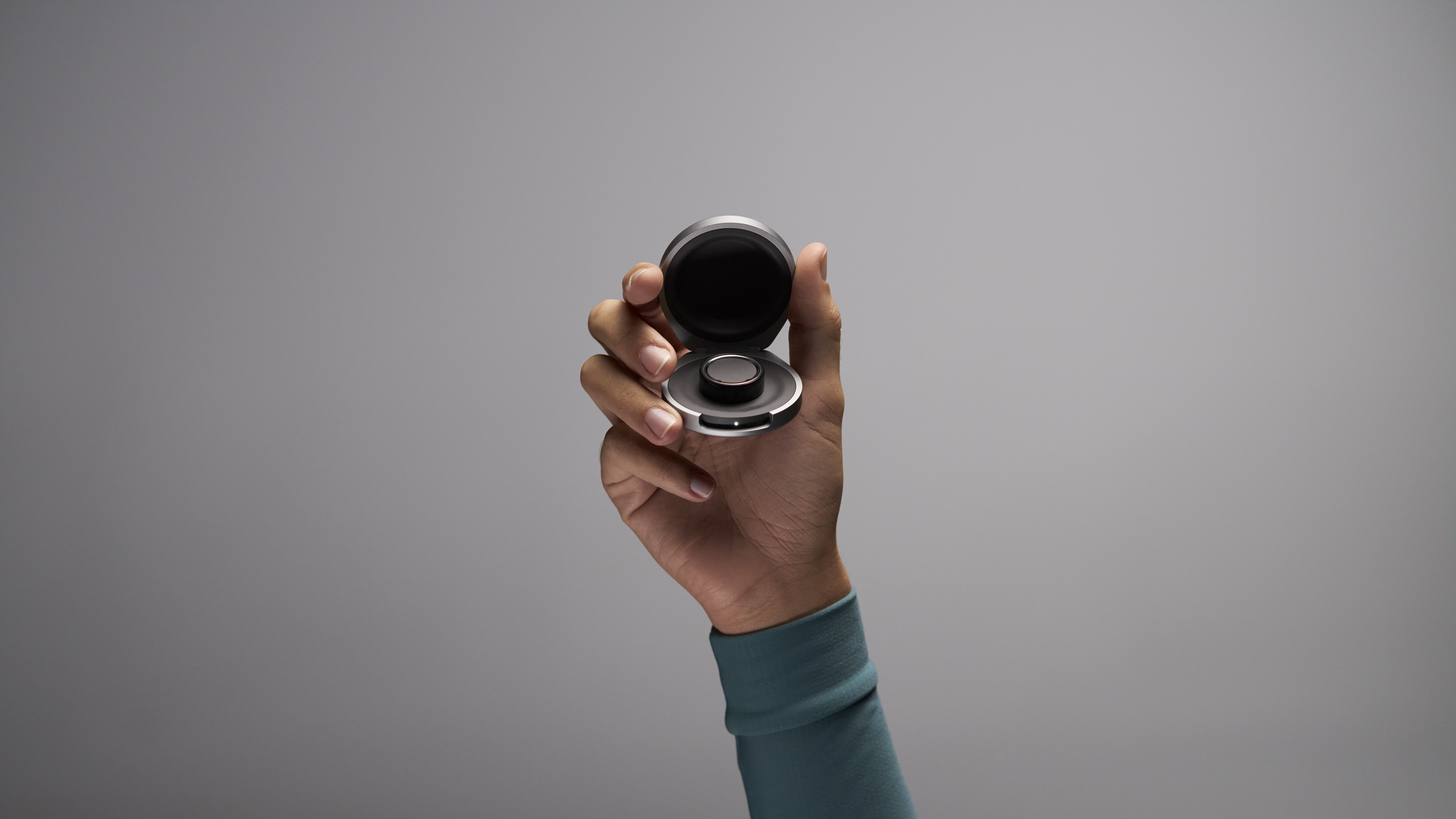 The Oura portable charging case being held up by a model with a Ring 4 inside.