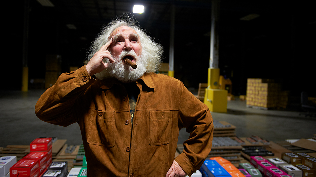 Mike Matthews from Electro-Harmonix posing with a cigar in front of stacks of pedals in boxes