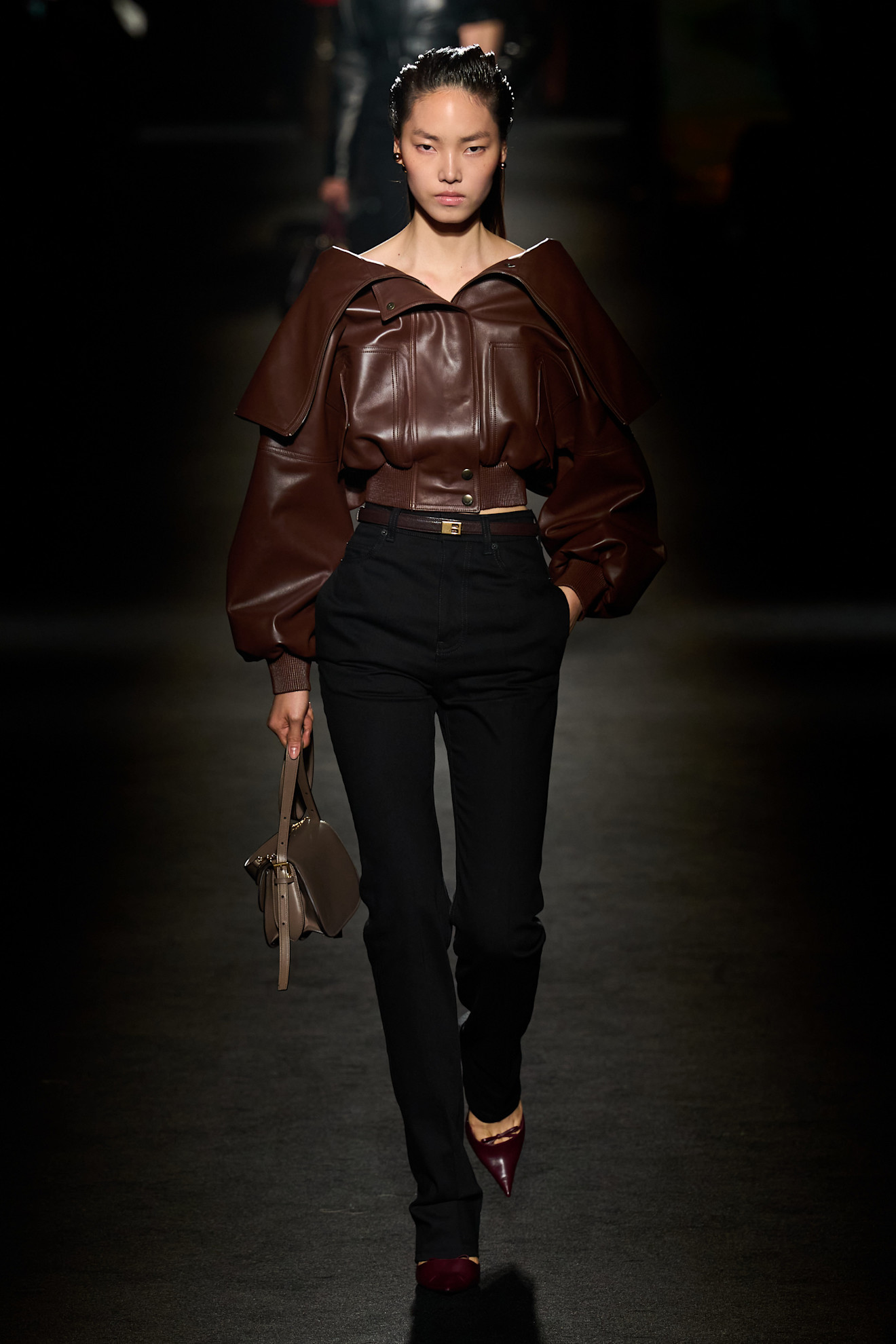 A model walking in the F/W 26 Balenciaga show during Paris Fashion Week wearing a leather cropped bomber jacket with black cigarette jeans and pumps.