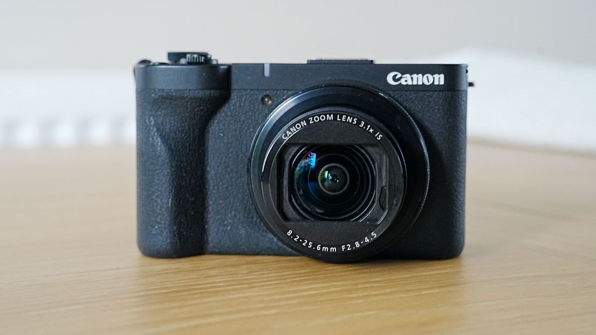The Canon Powershot V1 on a wooden table with shutter open and facing camera.