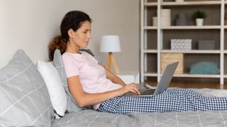 Woman laying in bed buying a new mattress on her laptop