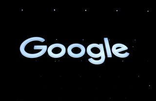 Google: A low-down shot of an illuminated pale blue Google logo, hanging from the ceiling in a pitch black room