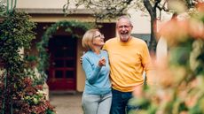 An older couple look happy as they walk away from a home arm in arm.