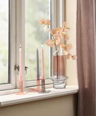 A windowsill with pink and gray candlesticks and a vase of pink flowers