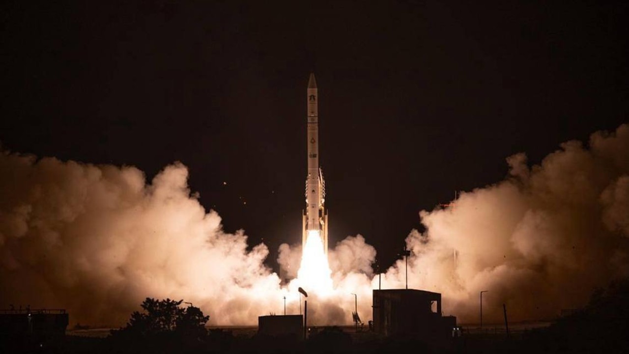 a white rocket launches at night above a plume of fire and smoke