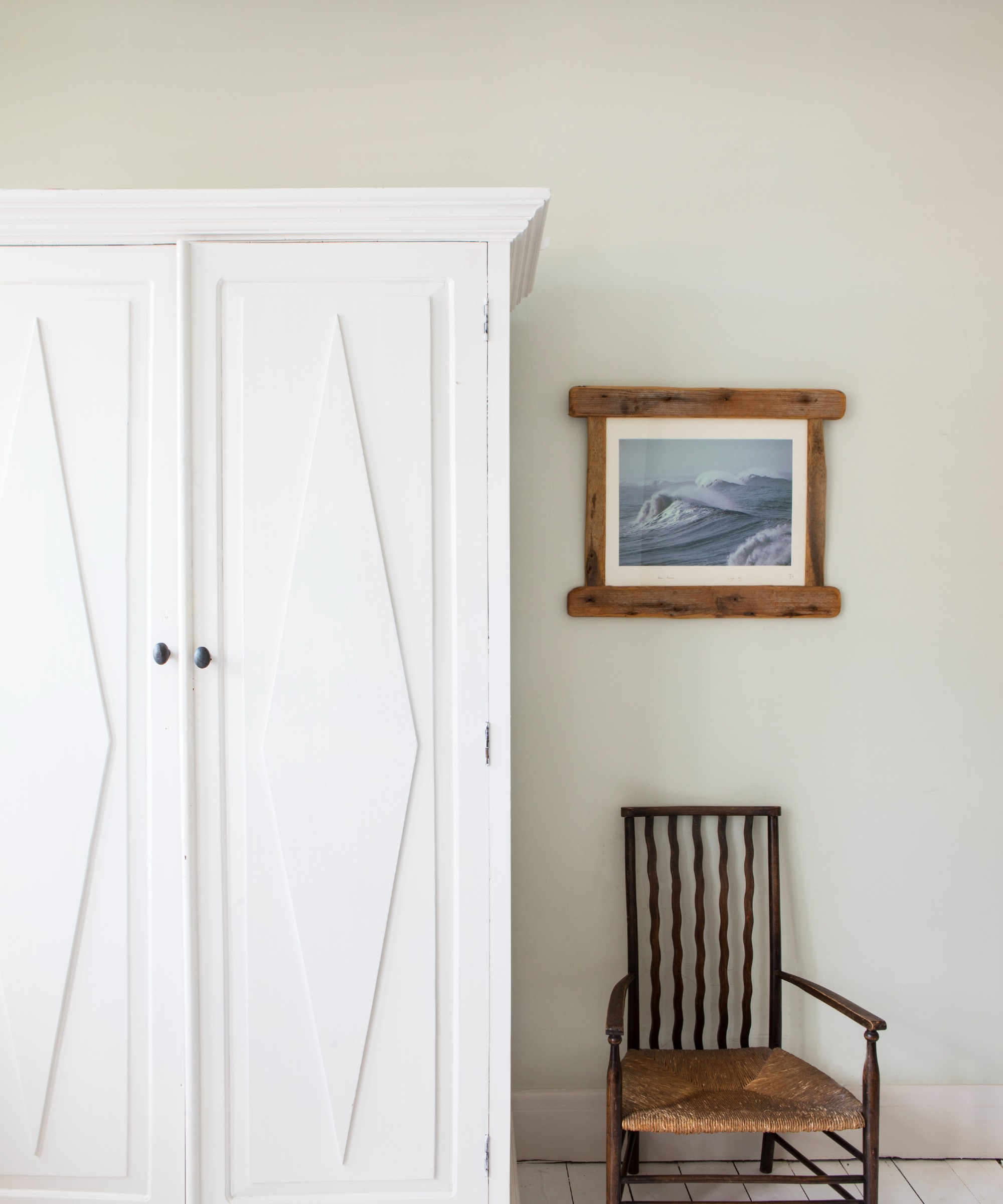A bedroom with off-white walls, a white wardrobe and an antique chair