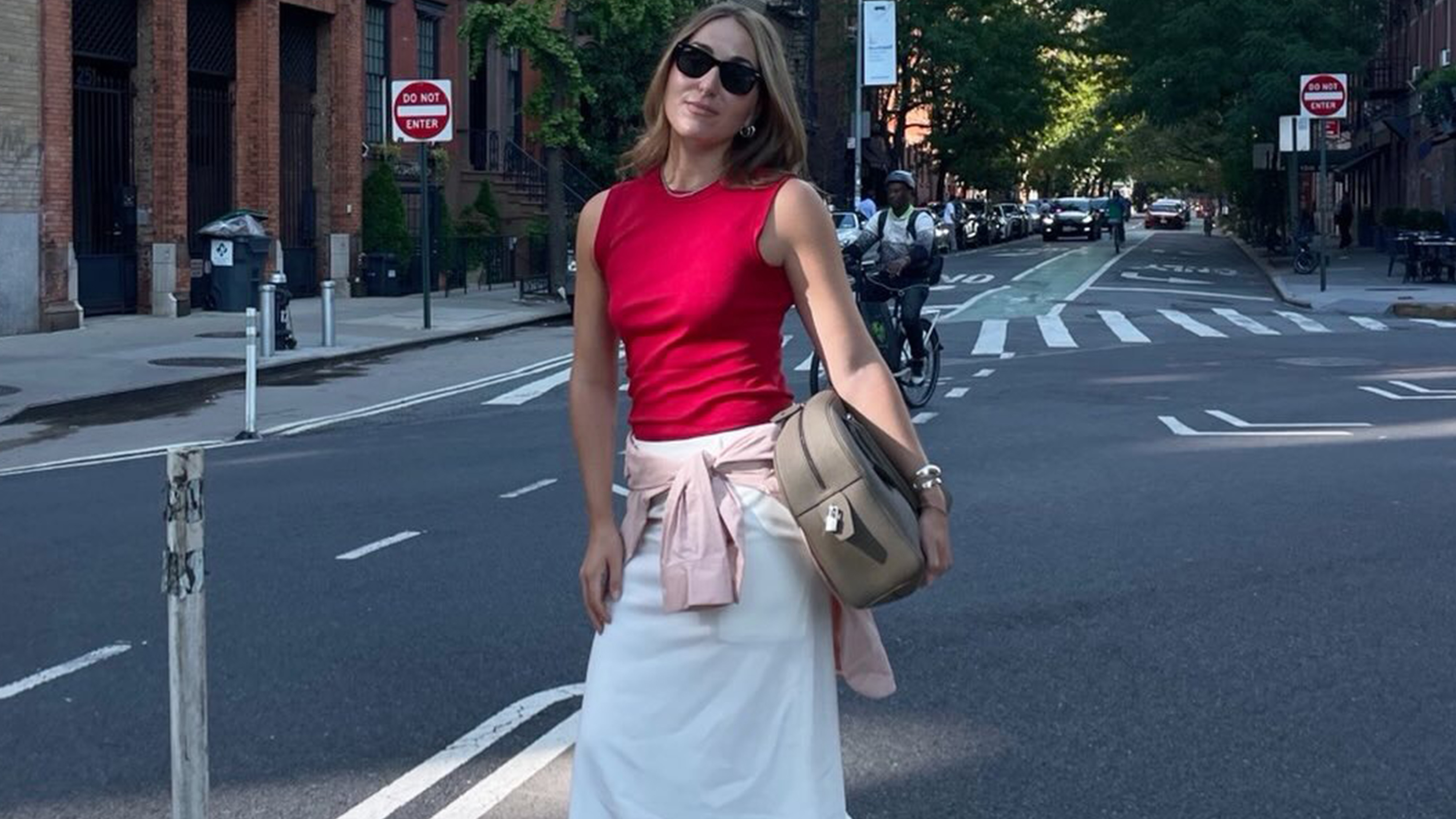 Anna wears a red top, white skirt and beige bag.