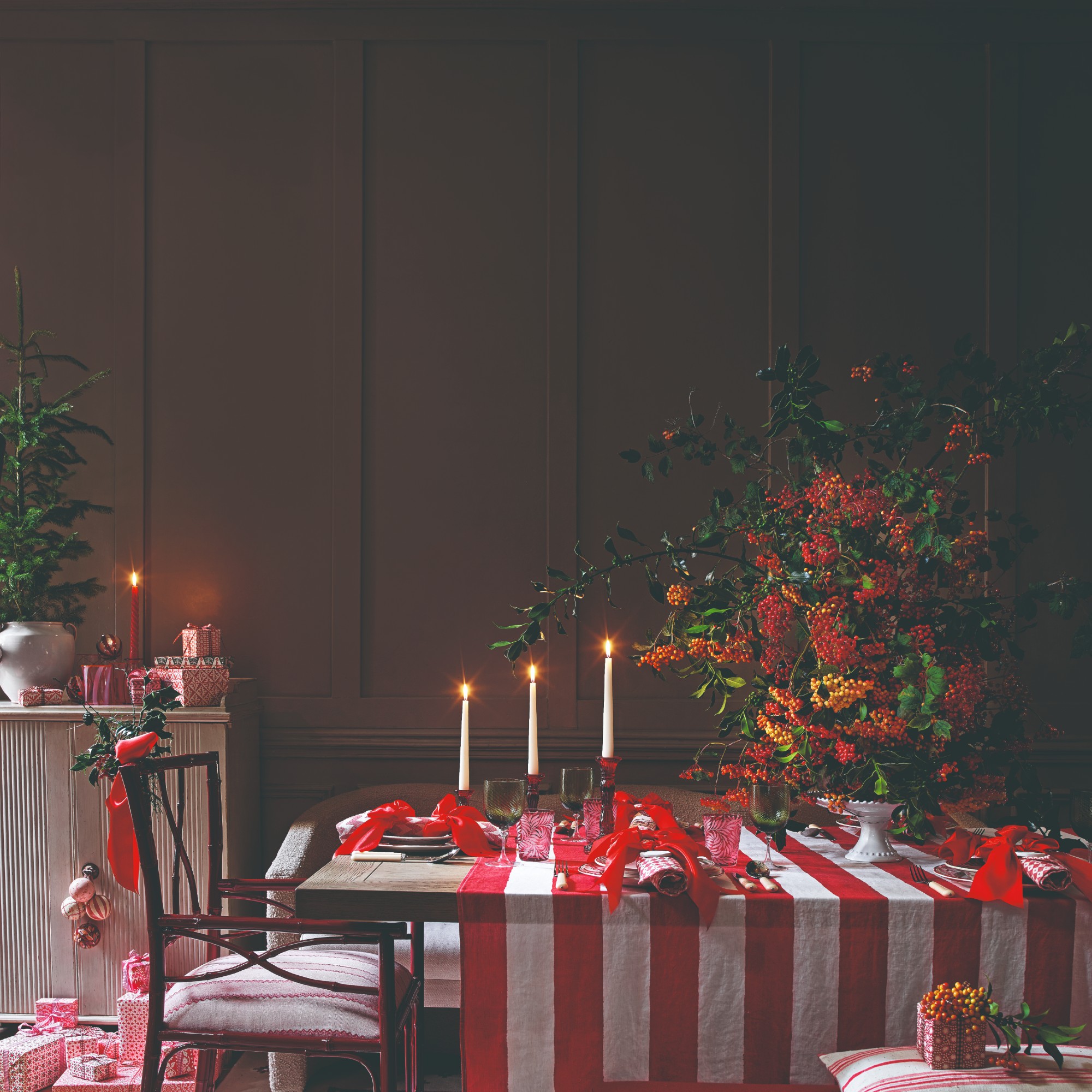 A dining table set and decorated for Christmas with a large centrepiece, dinner candles and red bows