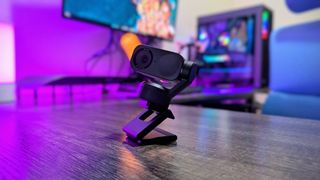 The Insta360 Link 2 webcam on a desk with violet backlighting, attached to its magnetic stand and extended.