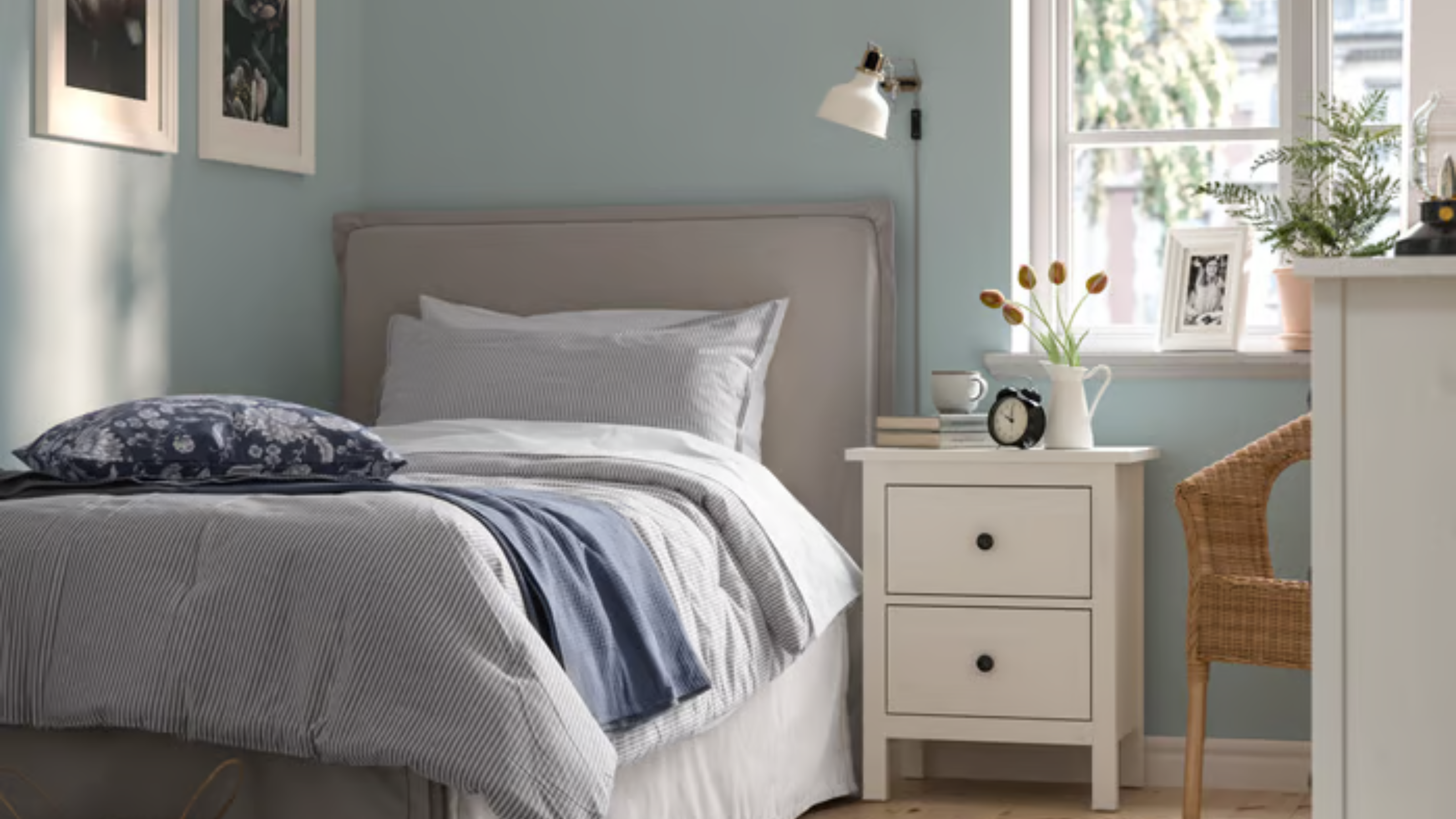 Coastal cool dorm room featuring pinstriped bedding, a white nightstand, woven accent chair, and framed artwork