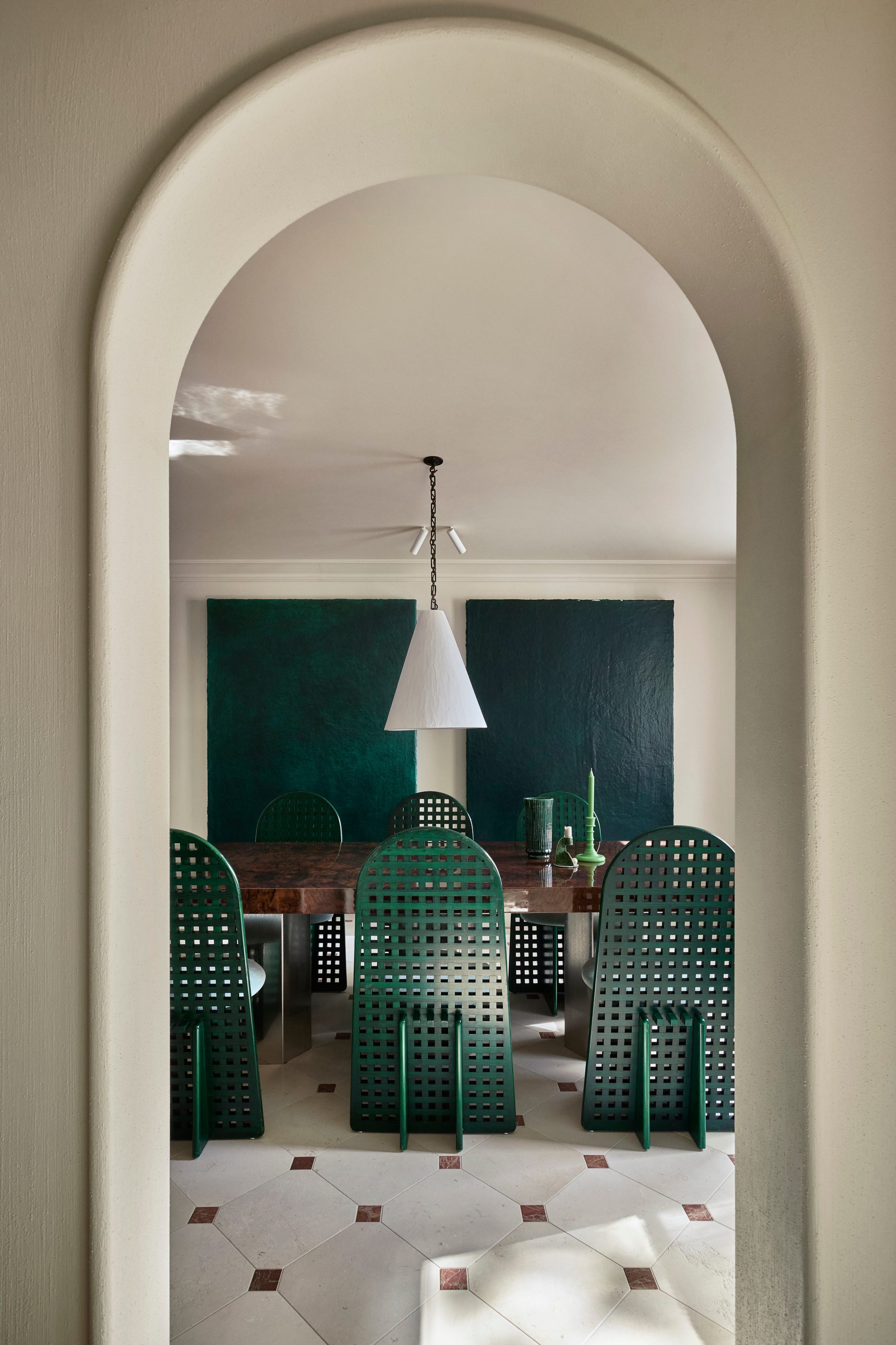View through archway to dining room with emerald green chairs, wood dining table, dark green artworks and white pendant light