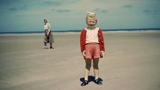 Old image of young child at beach with woman in background